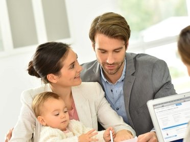 A young family of three talking to a woman with a laptop.